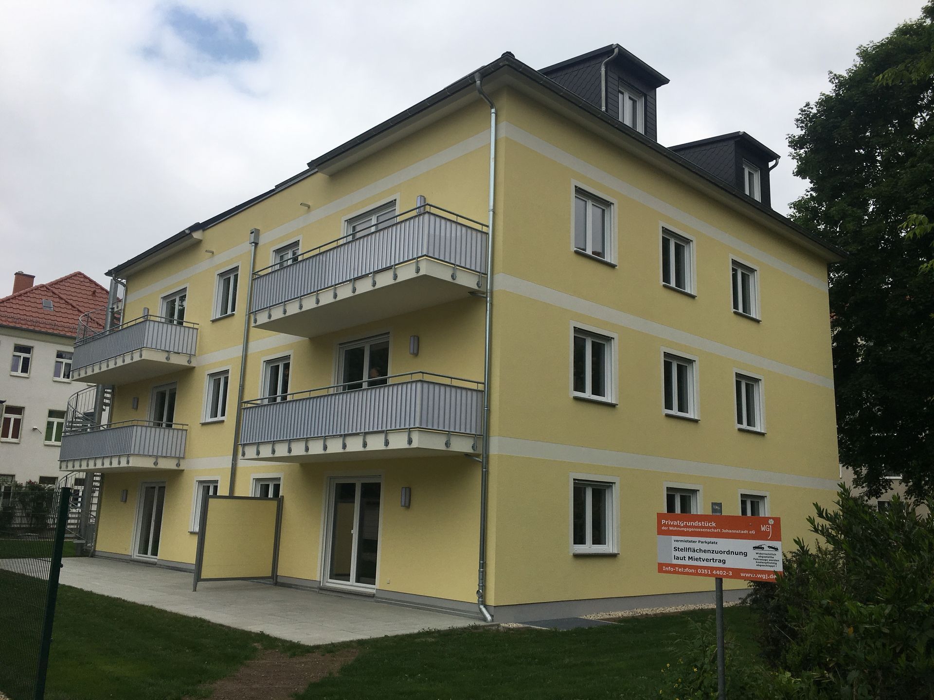 Gelbes Mehrfamilienhaus im Außenbereich mit Hinweisschild im Vordergrund
